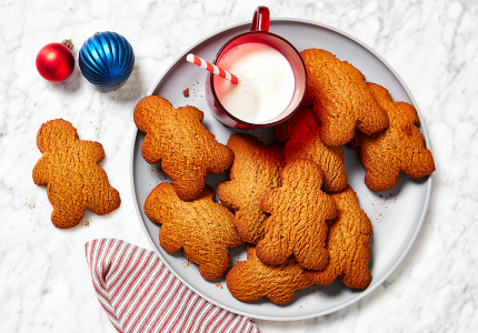 A round grey serving plate topped with gingerbread people, a red mug of milk, and a striped napkin.