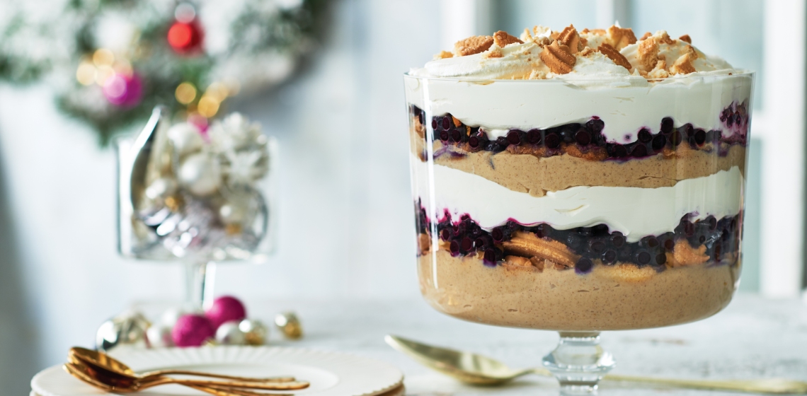 A glass trifle bowl filled with layers of pudding, cookies, cream, and fruit.