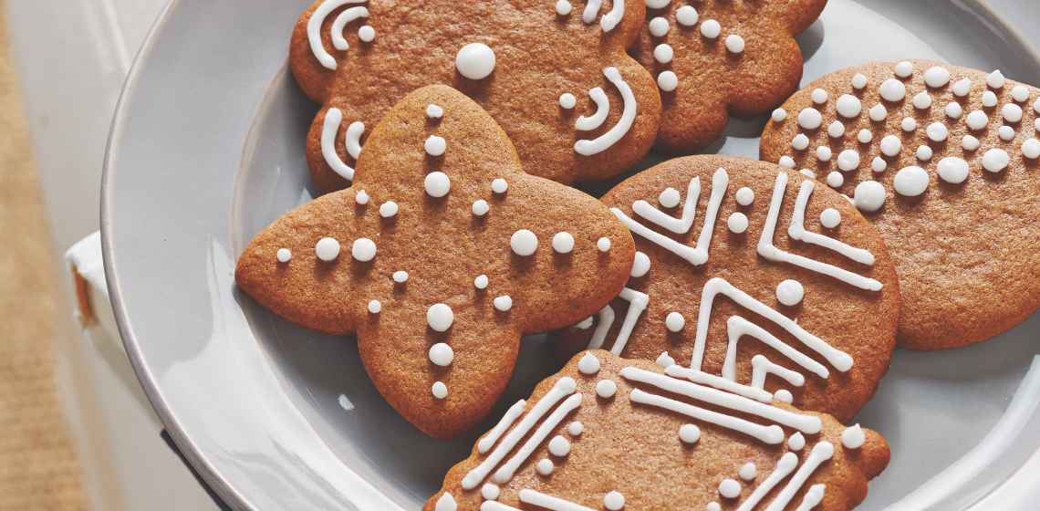 A white plate of gingersnap cookies with royal icing decoration on top.