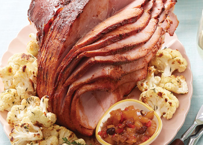 Sliced ham on pink plate with small bowl of pineapple chutney surrounded by vegetables