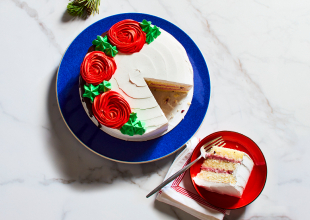 Round blue platter with Merry Berry Cake with white icing, green icing leaves and red icing roses on top