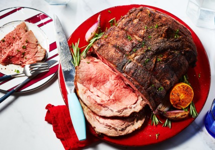 round red serving platter with moroccan-spiced roast beef, with slices cut on one end, and a rosemary and citrus garnish on the side