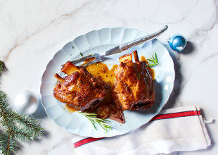 White scallop-edge platter with two large roasted pork shanks with sauce and sprinkle of rosemary