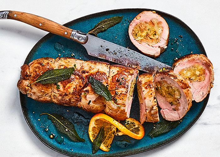 Top-down image of marble countertop with blue serving platter of stuffed pork with a fried sage garnish on top.