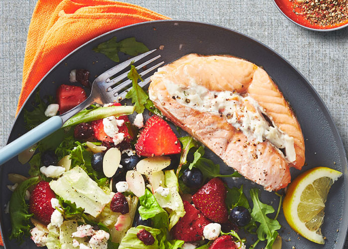 Black plate with salmon fillet and side salad