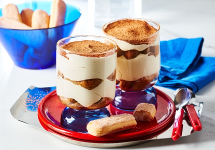 Small red serving tray with two Individual cups of tiramisu trifle, layered with espresso-soaked ladyfingers, mascarpone cream and cocoa sprinkle.