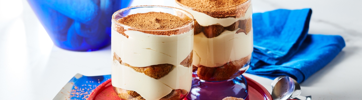 Small red serving tray with two Individual cups of tiramisu trifle, layered with espresso-soaked ladyfingers, mascarpone cream and cocoa sprinkle.