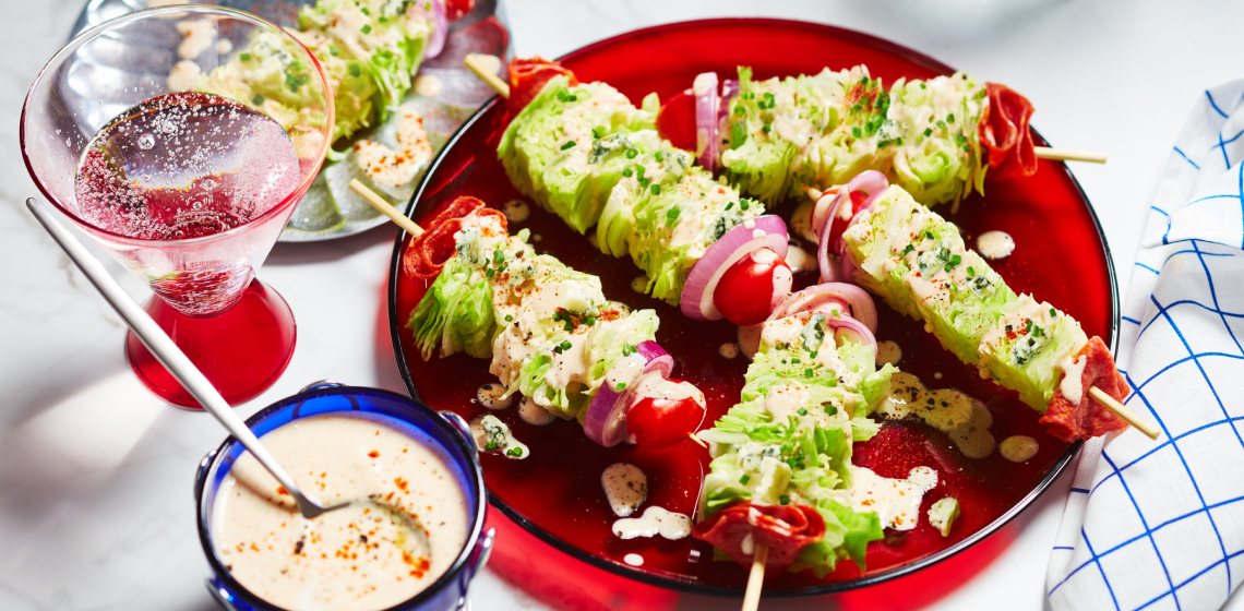 Red serving platter with five wedge salad skewers, and a side dish of dressing with a spoon dipped in