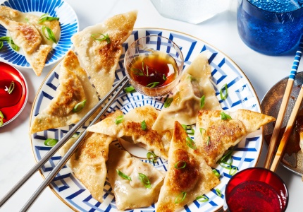 Decorative white and blue plate with gold rim topped with chicken potstickers, chopsticks and small bowl of dipping sauce