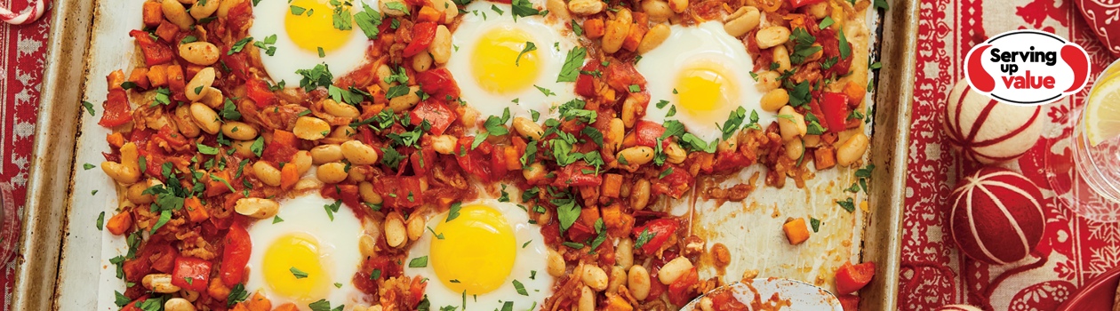 Baking sheet pan of bacon, beans and eggs breakfast on a set table with a red patterned tablecloth.