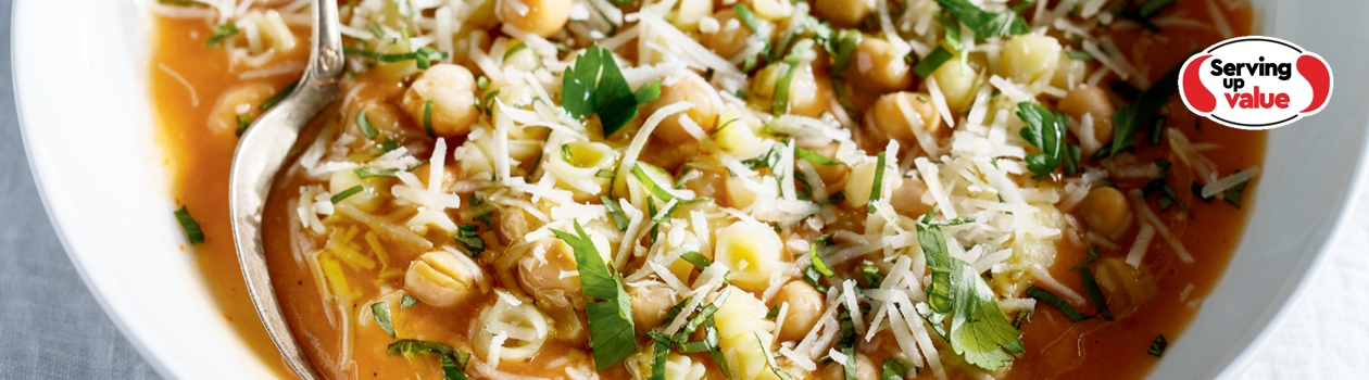 White soup bowl of pasta and chickpea ragu with side slices of baguette and soup spoon dipped in.