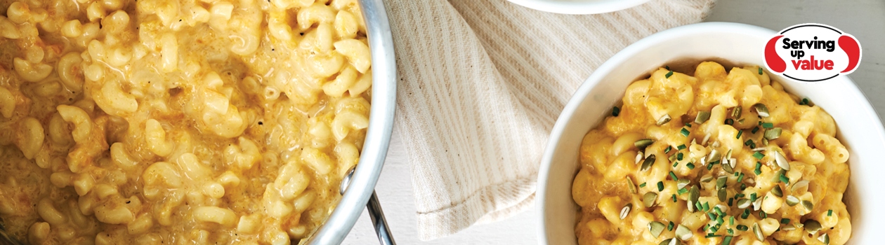 Stainless steel pot of butternut squash macaroni and cheese with two side bowls filled with pasta and a pistachio garnish.