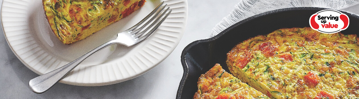 Cast iron skillet of zucchini and sun-dried tomato frittata with slices taken; servings shown to the side on side plates with fresh arugula salad.