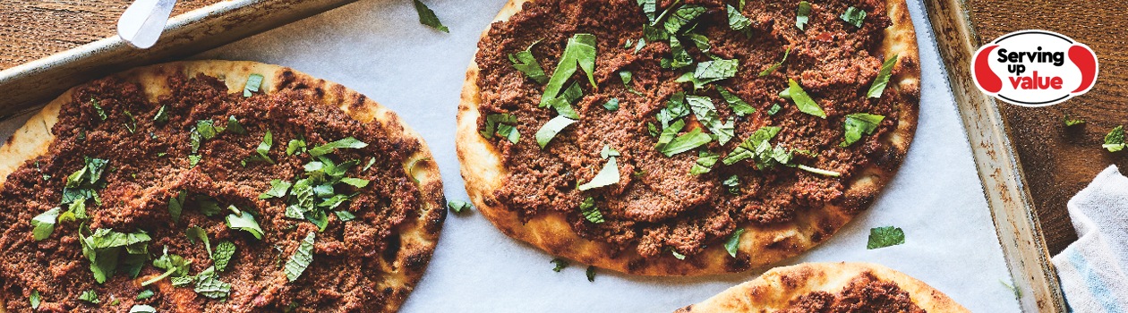 Baking sheet with four meat-topped flatbreads garnished with fresh mint and parsley